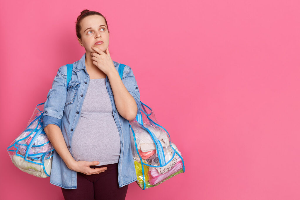 mulher grávida pensando o que levar para maternidade segurando duas malas 