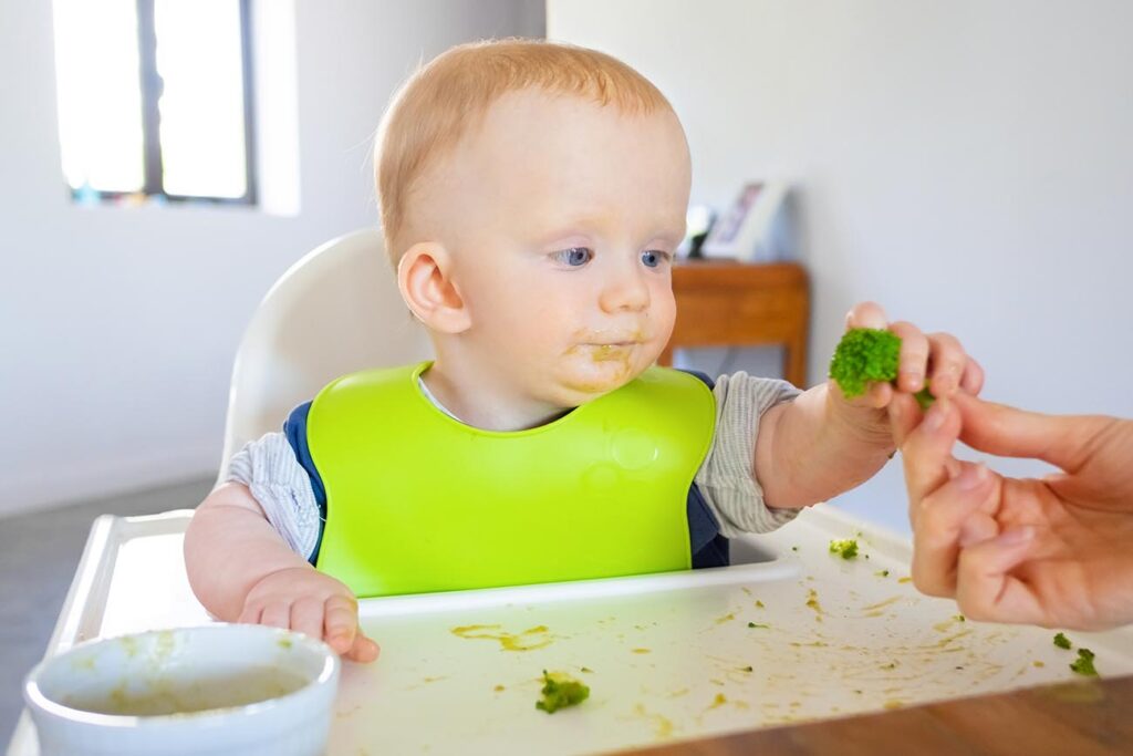 Bebê com Sinais de Prontidão para Introdução Alimentar segurando um brócolis