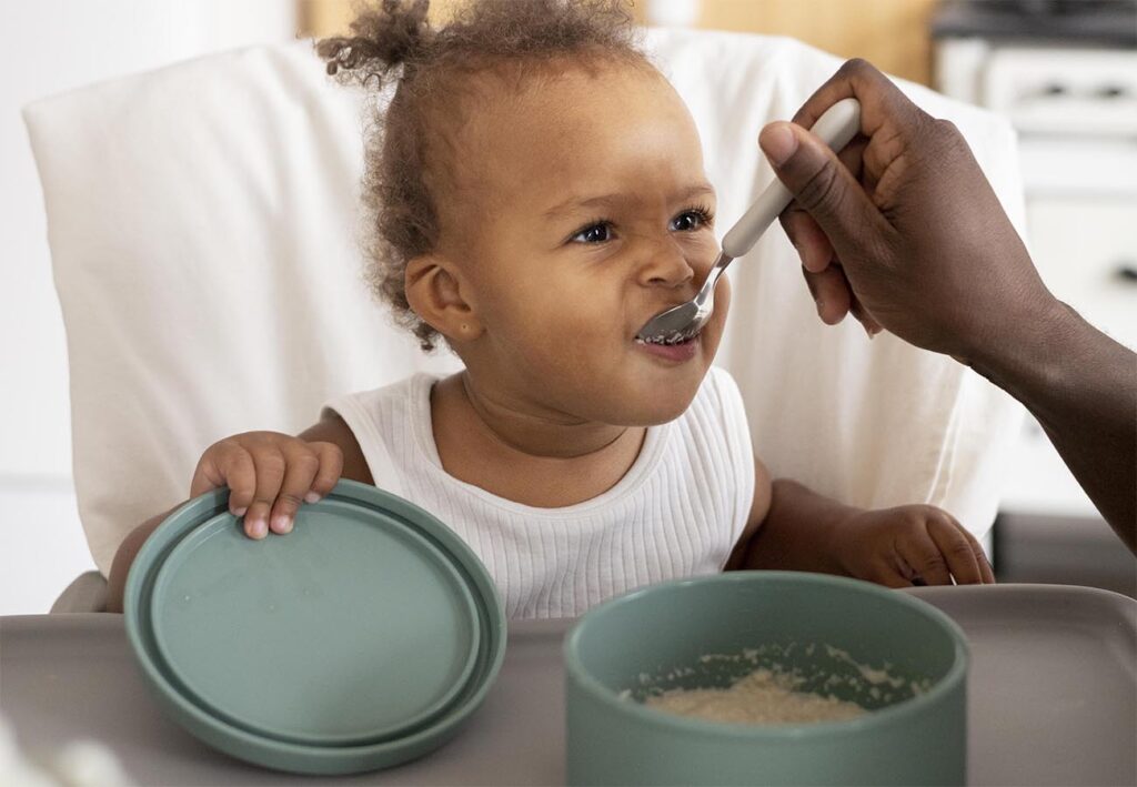 Bebezinha comendo papinha de aveia apresentando sinais de prontidão para introdução alimentar