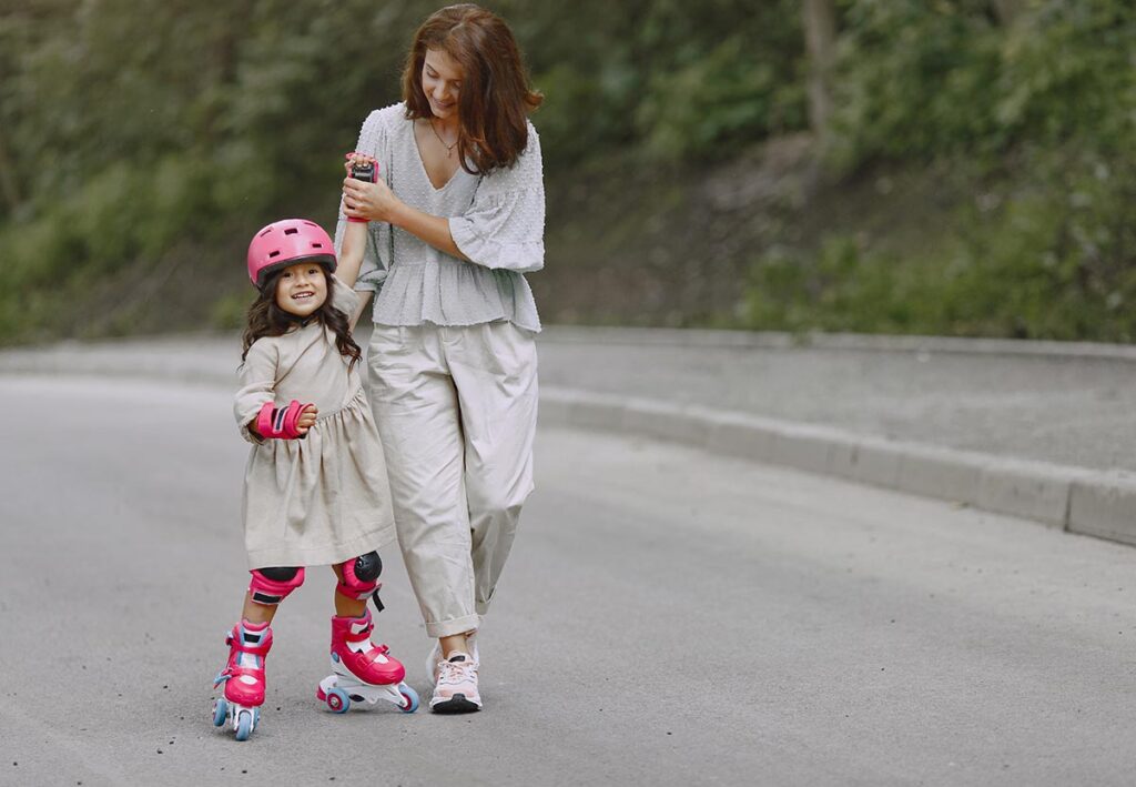 Criança de patins com equipamentos de segurança de mãos dadas com a mãe